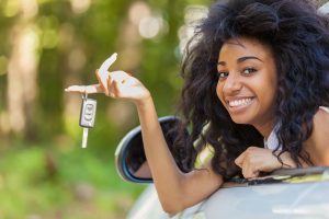 Young beautiful black teenage driver holding car keys driving her new car